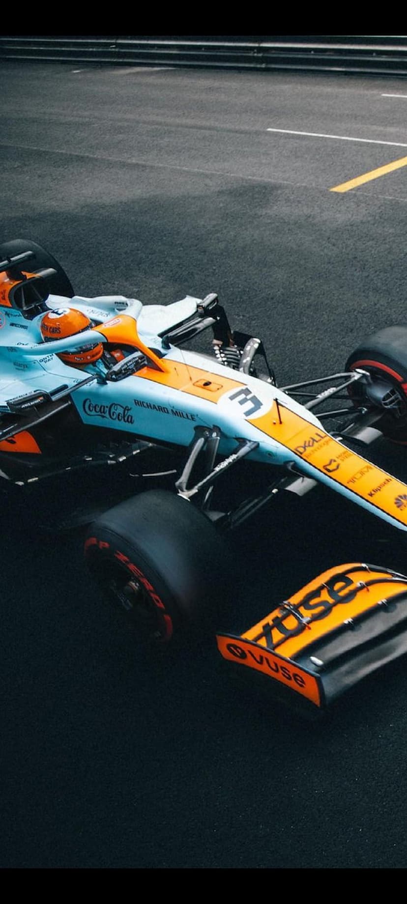 McLaren Formula 1 car with orange livery drives on a race track with yellow markings and sponsor decals.