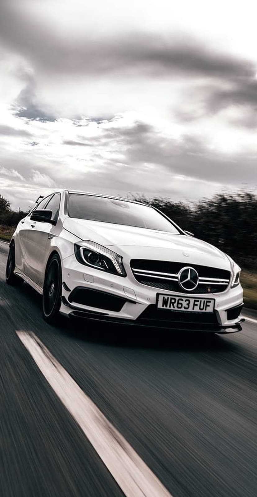 White Mercedes-Benz AMG hatchback in motion on a road featuring black wheels and a visible license plate.