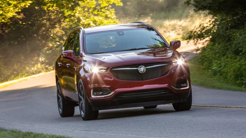 Red Buick Enclave SUV driving on a winding forest road with golden sunlight and lush green trees.