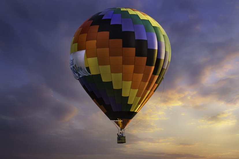 Multi-colored hot air balloon ascending through dark sunset clouds with warm golden light illuminating the sky.