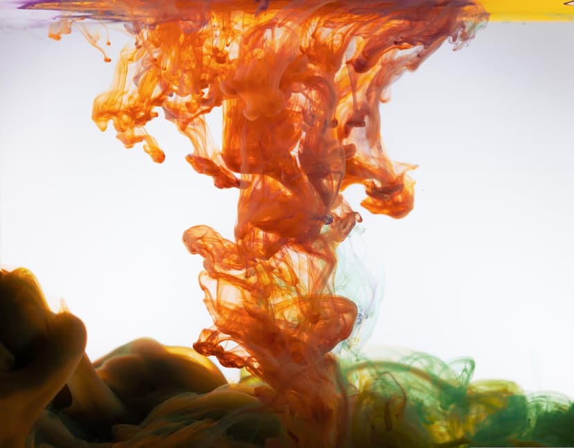 Orange and green ink clouds dispersing in water with intricate swirling patterns and microscopic fluid bubbles.