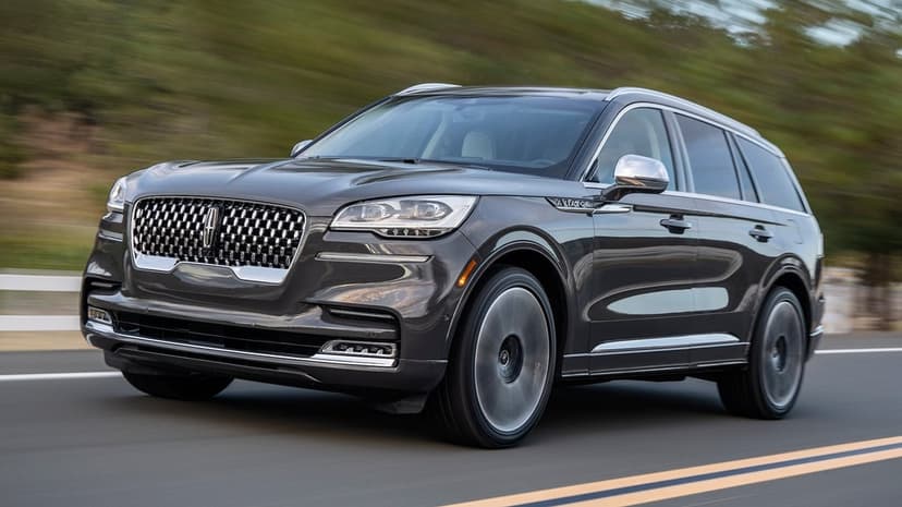 Charcoal Lincoln Aviator SUV driving on a highway with motion-blurred green trees and a scenic background.
