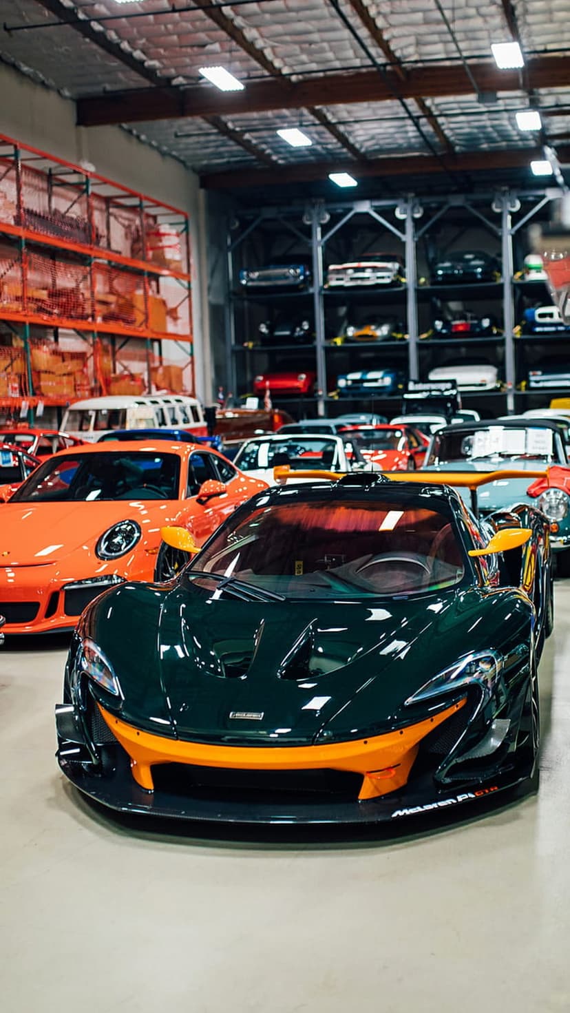 Orange and green sports cars parked in a multi-level glass showroom with modern industrial storage racks.