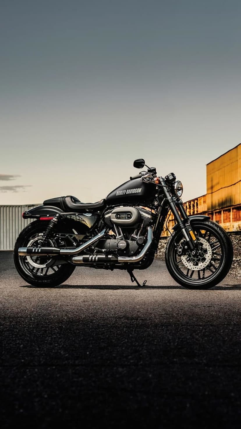 Black Harley-Davidson motorcycle with chrome exhaust parked on an asphalt road by a weathered brick building.