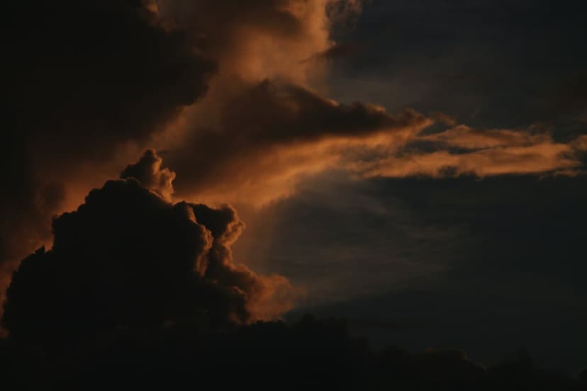 Sunlit storm clouds with golden edges and dark silhouettes fill a vertical twilight sky with dramatic textures.