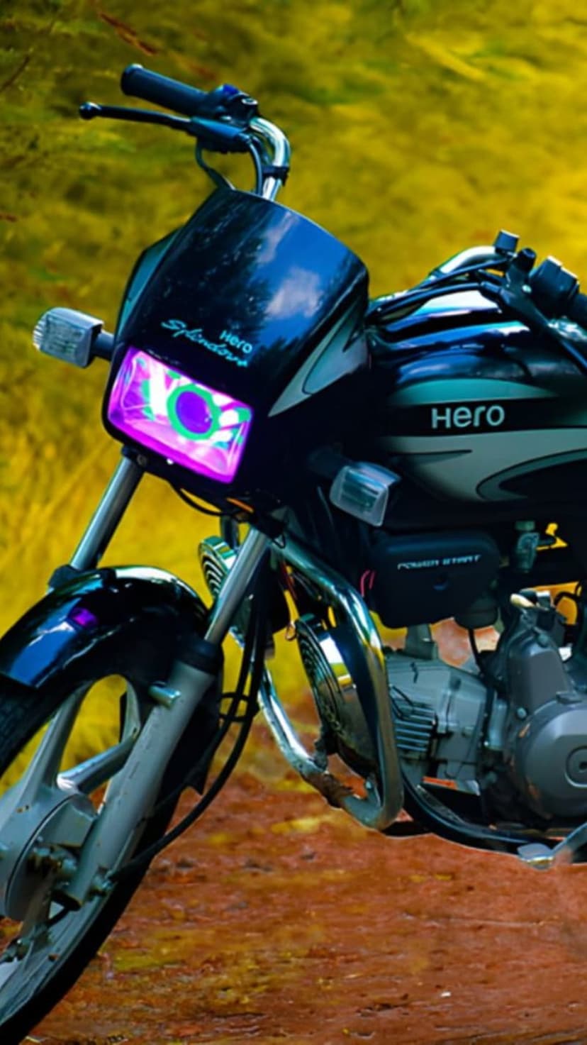 Hero Splendor motorcycle with a glowing purple and green LED headlight against a blurred outdoor background.