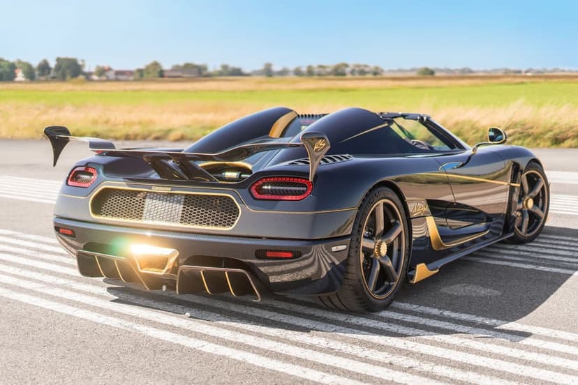Rear view of a blue carbon fiber Koenigsegg Agera RS with gold leaf accents on a sunny airfield runway.