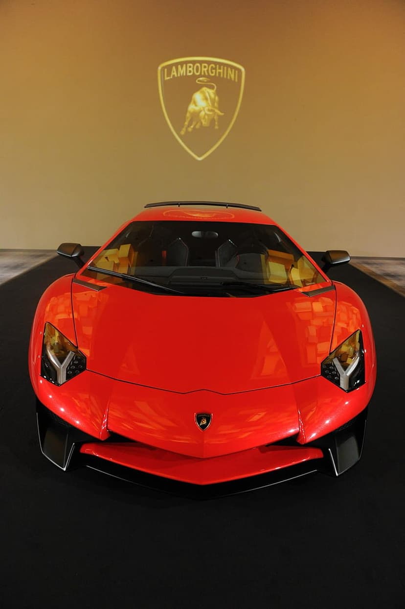 Red Lamborghini Aventador front view with a glowing gold charging bull logo projected on the dark back wall.