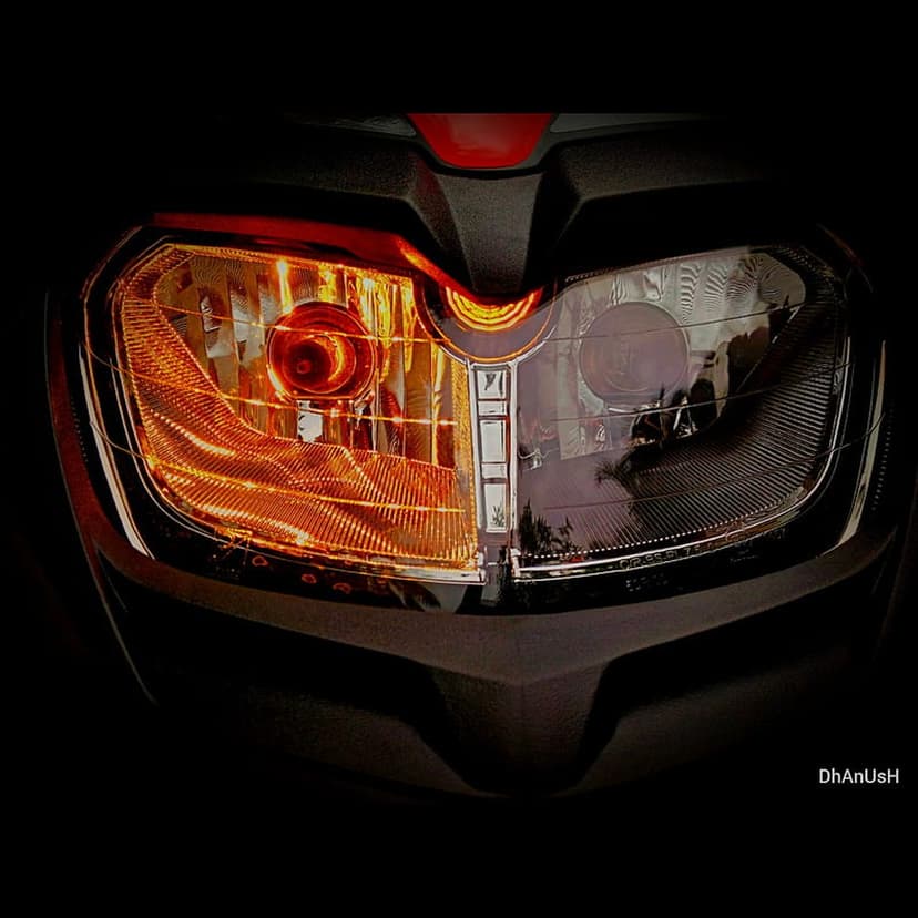 Motorcycle headlight with an orange bulb glow, textured reflector, and black fairing against a dark background.