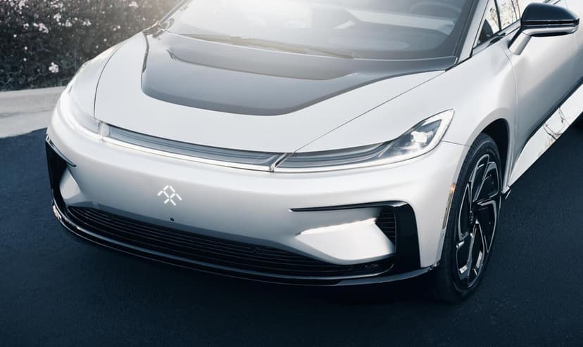 Front view of a white Faraday Future FF 91 electric car with glowing logo and slim LED headlights on asphalt.