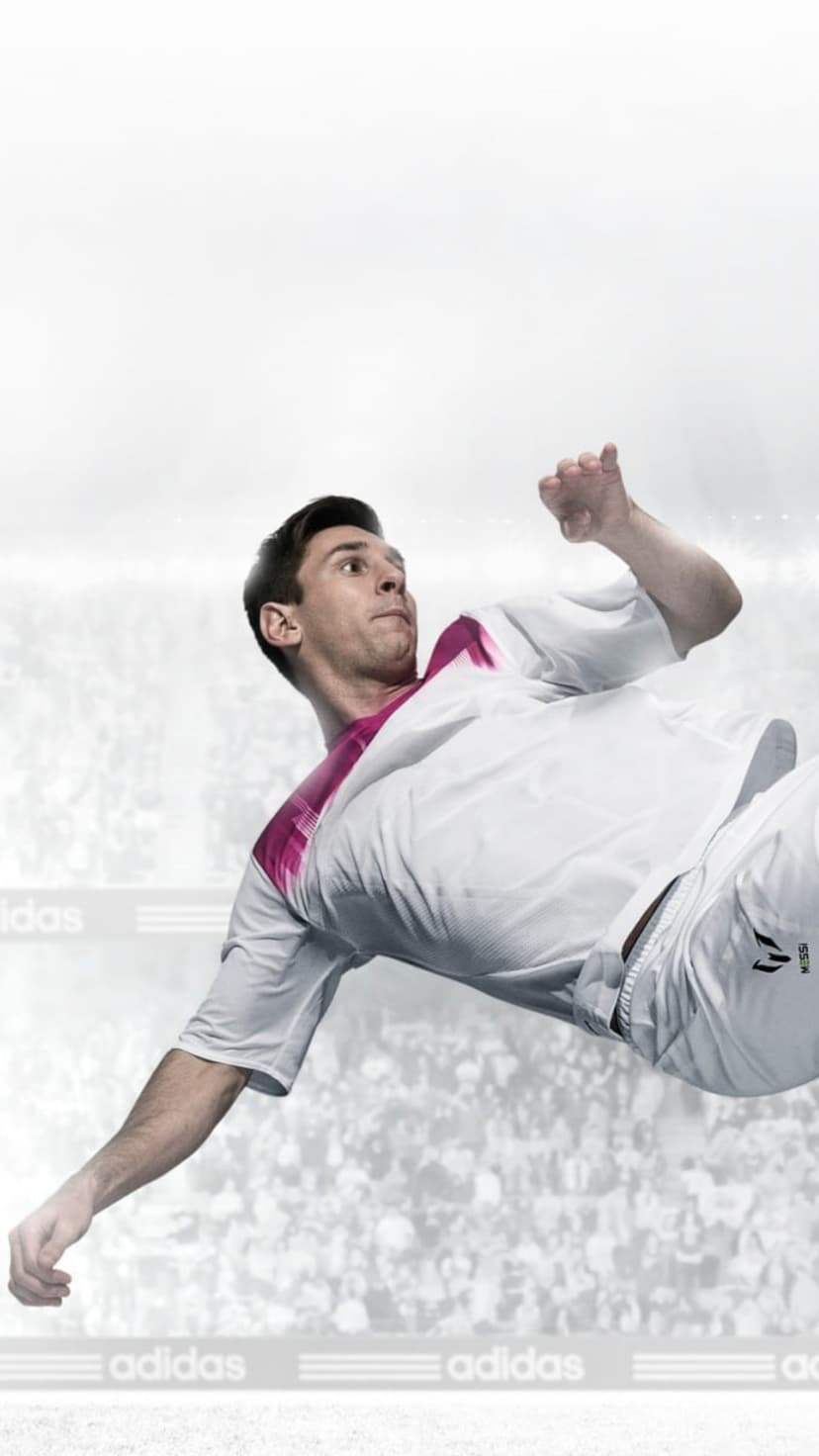 Lionel Messi leaps mid-air wearing Adidas soccer gear against a blurred stadium crowd during a match.