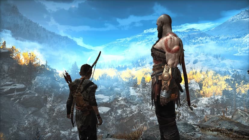 Kratos and Atreus stand on a cliff overlooking a snowy mountain valley with golden trees and blue sky.