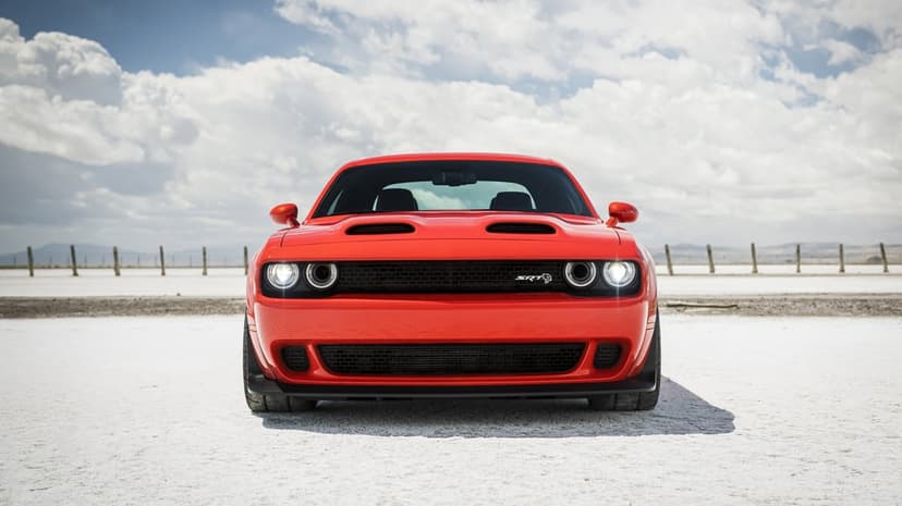 Red Dodge Challenger SRT Hellcat Redeye on a white salt flat under a cloudy blue sky in front-facing view.