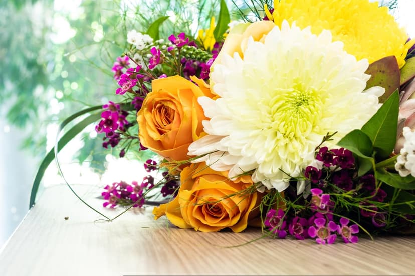 Orange roses and a white chrysanthemum rest on a wooden table with a soft-focus green garden background.