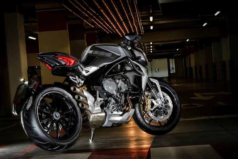Silver MV Agusta Brutale 800 motorcycle with triple exhaust in a dark industrial parking garage at night.