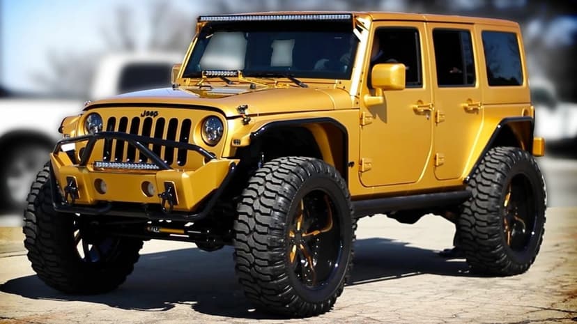 Golden modified Jeep Wrangler with large off-road tires and LED light bars parked outdoors on a sunny day.