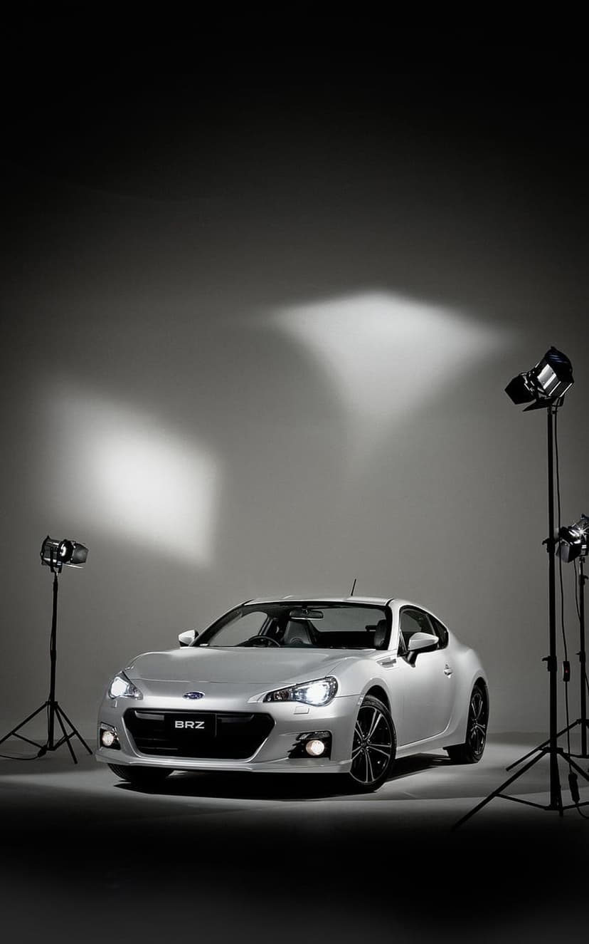 Silver Subaru BRZ sports car features dramatic studio lighting against a gray gradient background in portrait.