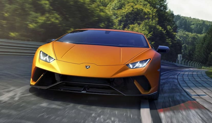 Orange Lamborghini Huracán Performante driving on a winding forest racetrack with glowing LED headlights.