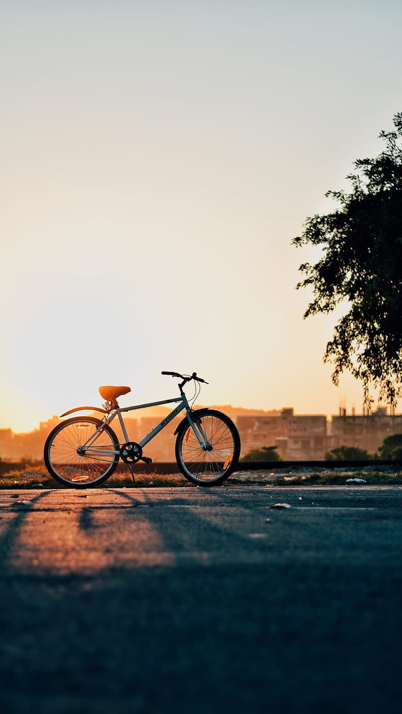 Bicycle silhouette stands on a quiet path against a glowing orange sky and sun during a warm evening sunset.