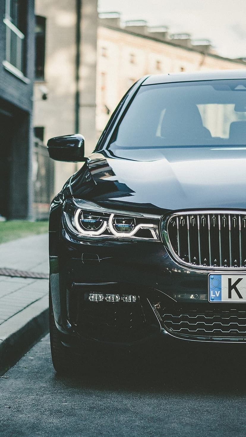 Black luxury sedan with illuminated LED headlights and a silver grille parked on an urban city street at night.