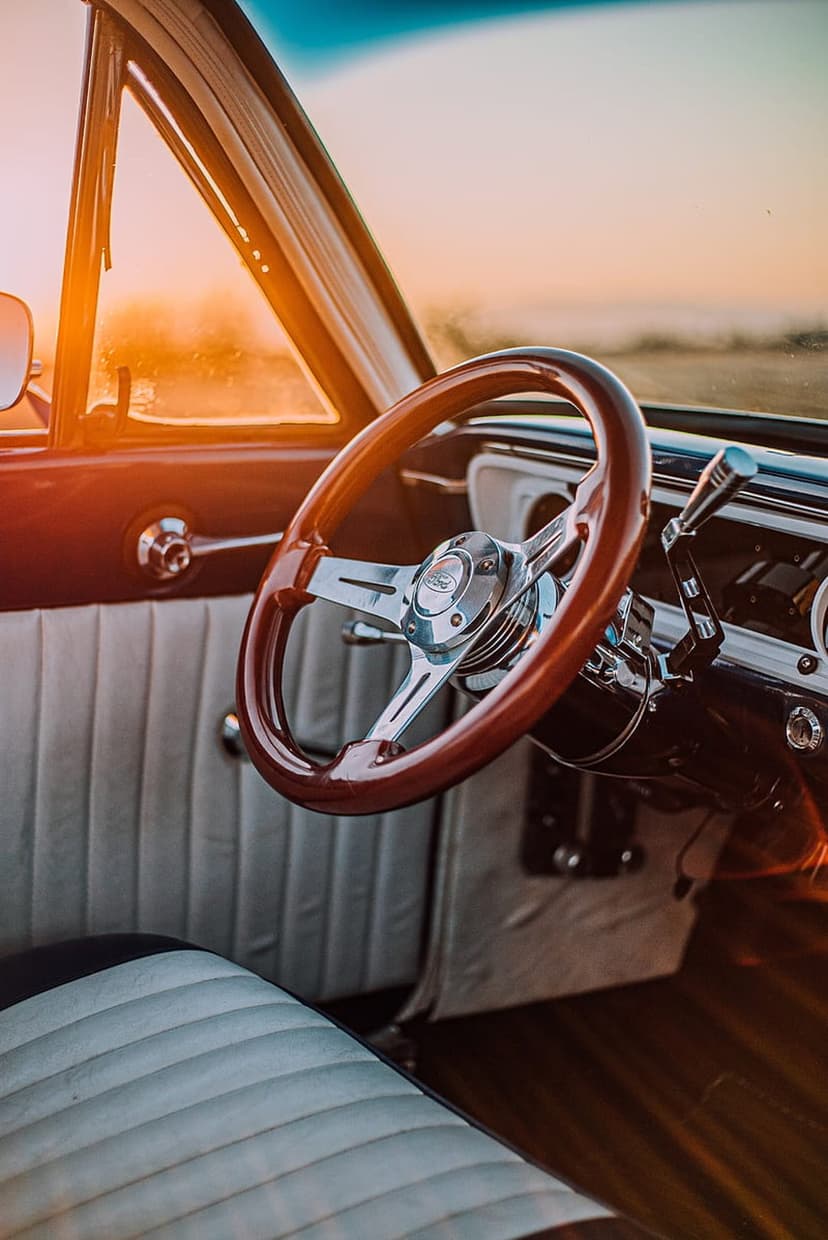 Polished wooden steering wheel and tufted leather seats inside a classic car bathed in warm sunset light.