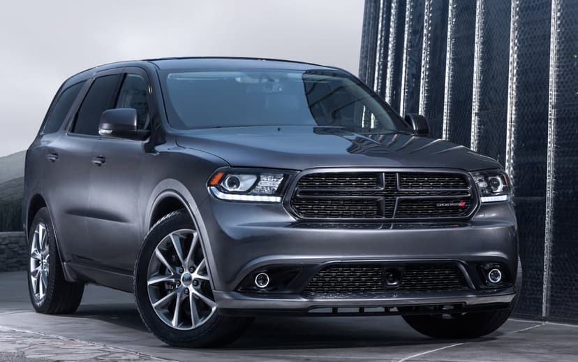 Metallic grey Dodge Durango SUV parked outdoors against a modern reflective building with bright LED headlights.