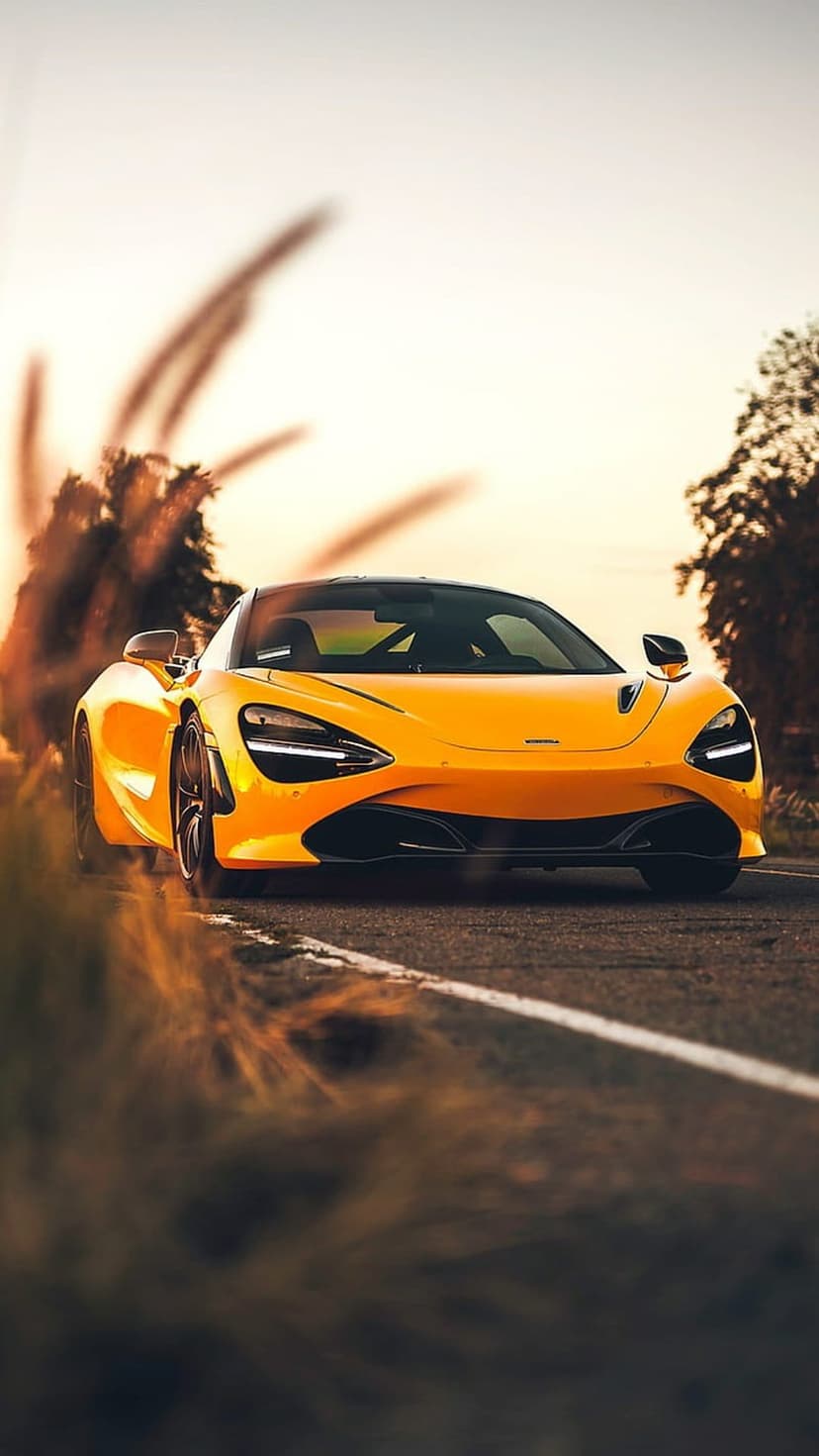 Yellow McLaren 720S sports car drives on a rural road during a golden sunset with long shadows and trees.