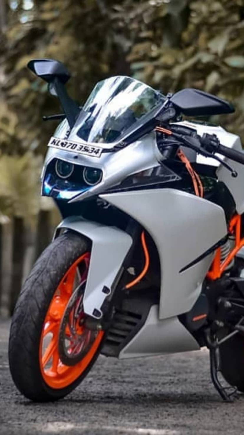 White KTM RC sportbike featuring vibrant orange rims and dual headlights parked outdoors in natural daylight.