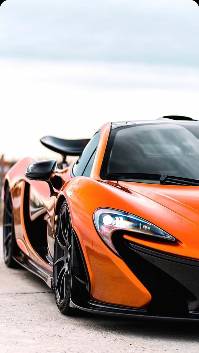 McLaren P1 supercar in orange with sharp headlights and a black spoiler against a soft blurred sky background.