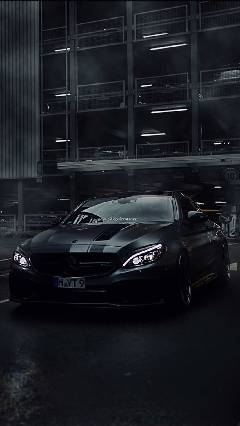 Mercedes-AMG C63 S Coupe with glowing LED headlights and racing stripes parked in a dark, atmospheric garage.