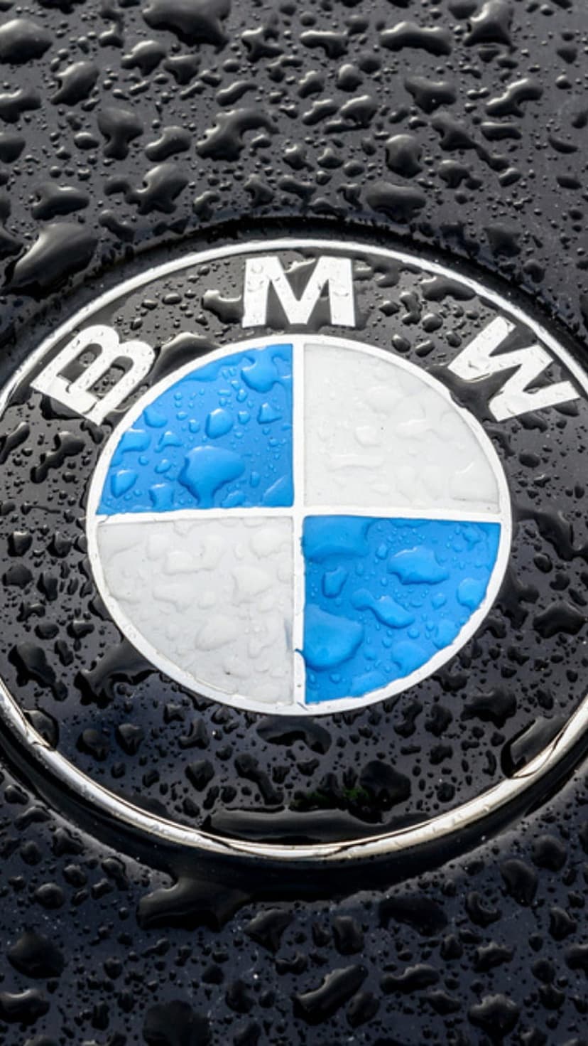 BMW emblem with blue and white quadrants covered in clear water droplets on a reflective black car surface.