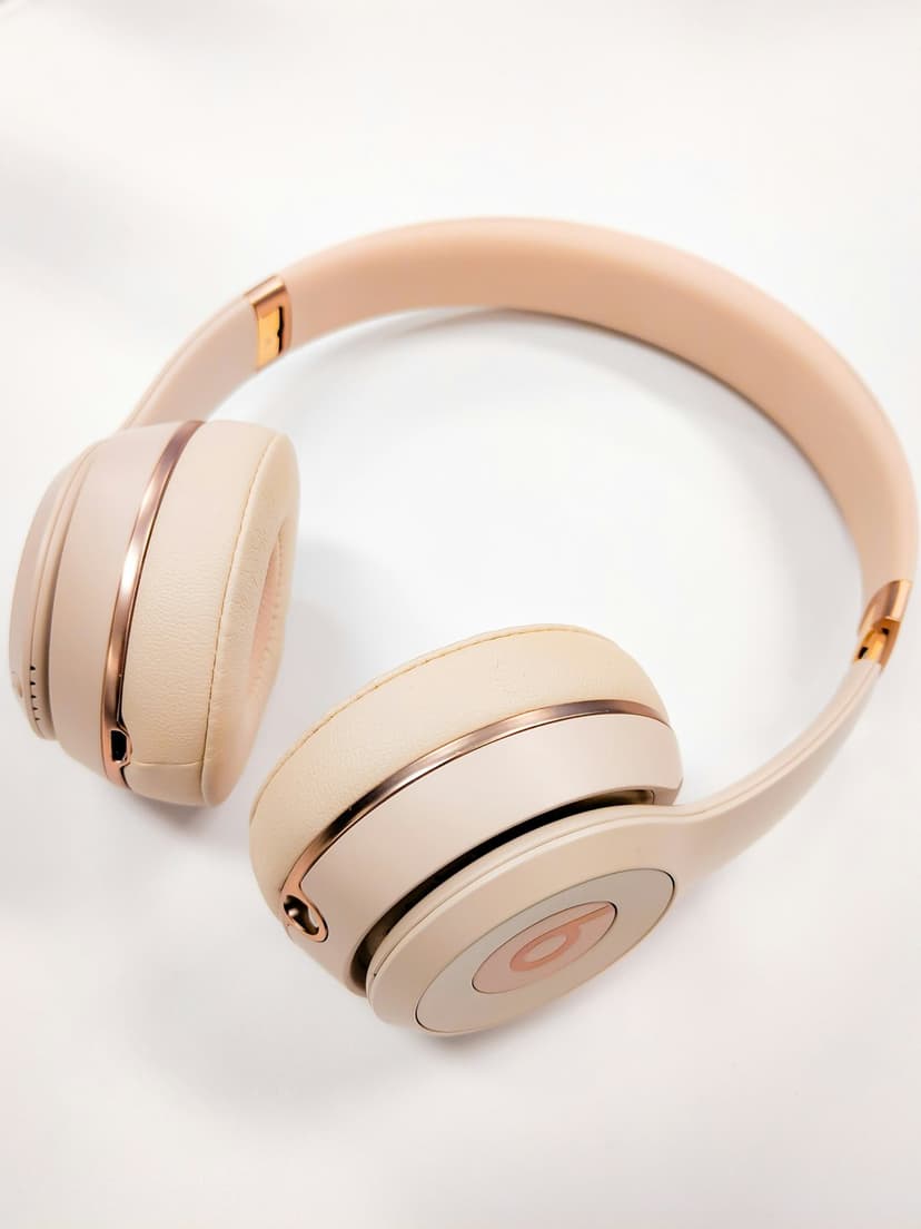 Rose gold wireless on-ear headphones with soft cushions and a metallic headband against a clean background.