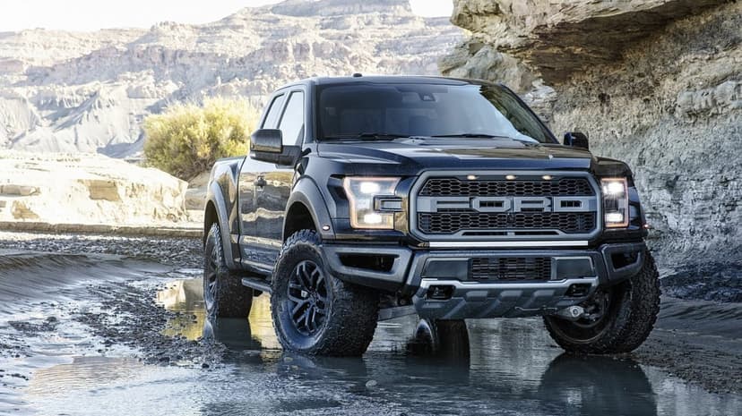 Black Ford F-150 Raptor parked in a rocky desert canyon with reflections in shallow water.