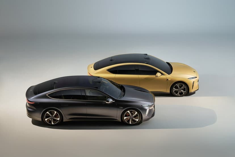 Charcoal grey and champagne gold electric sedans parked in a bright minimalist studio with soft shadows.