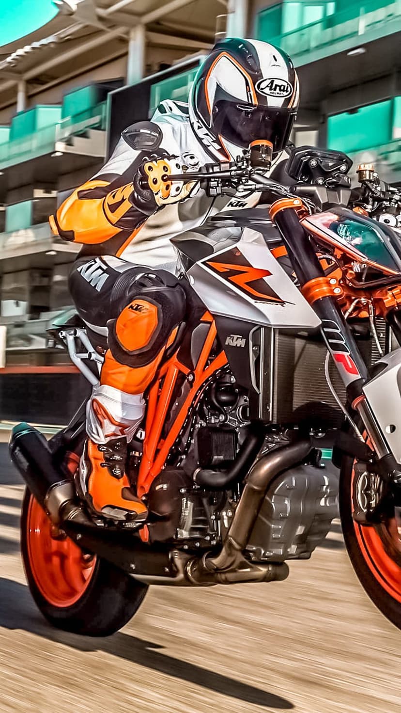 KTM racer in orange and white gear leans into a curve on a grey asphalt racing circuit during a track day.