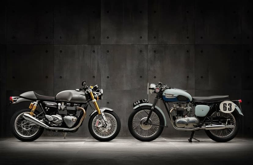 Modern grey Thruxton and vintage blue Triumph motorcycles against a dark paneled wall with studio lighting.