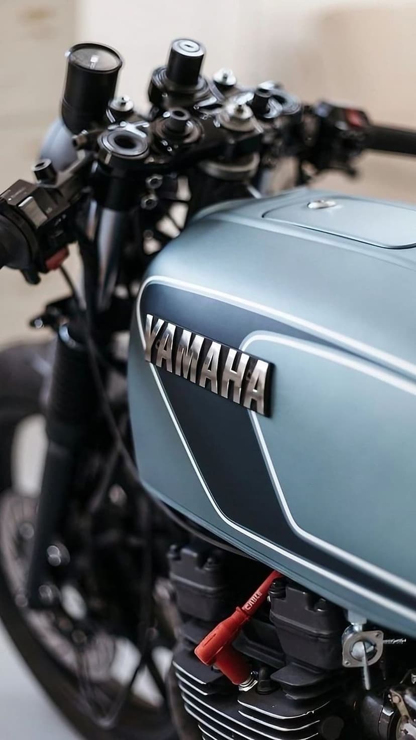 Chrome Yamaha logo on a pale blue fuel tank with handlebars and a red spark plug wire in sharp detail.