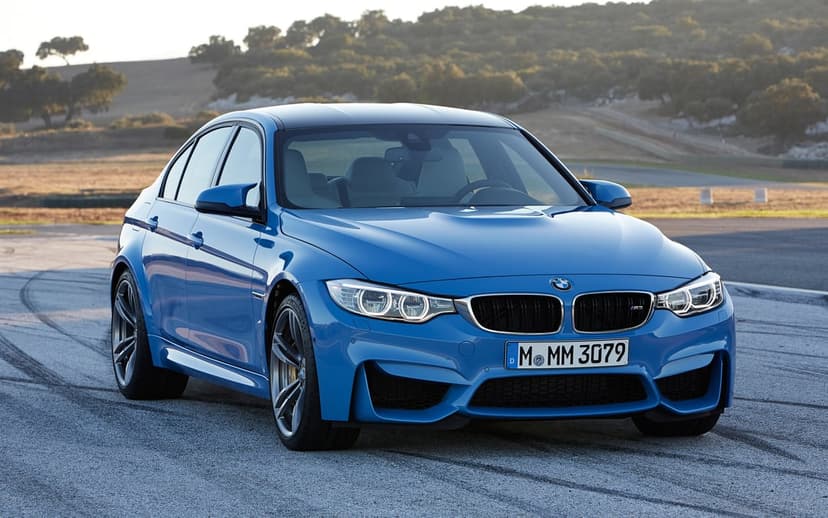 Blue BMW M3 sport sedan on an asphalt race track with tire marks and a soft sunset hill background.