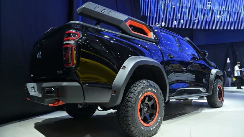 Rear view of a black off-road pickup truck with orange wheel accents and rugged tires on an exhibition stage.