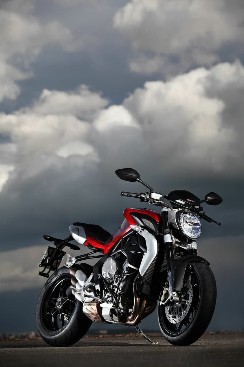 Red and black MV Agusta Brutale motorcycle on asphalt under a dramatic, dark cloudy sky at low angle.
