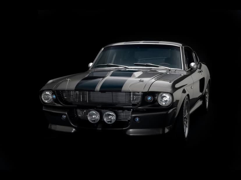 Silver Shelby GT500 with black racing stripes on a black background with dramatic studio lighting.