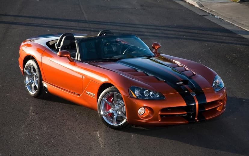 Orange Dodge Viper SRT10 convertible with black stripes on asphalt under warm sunset lighting.