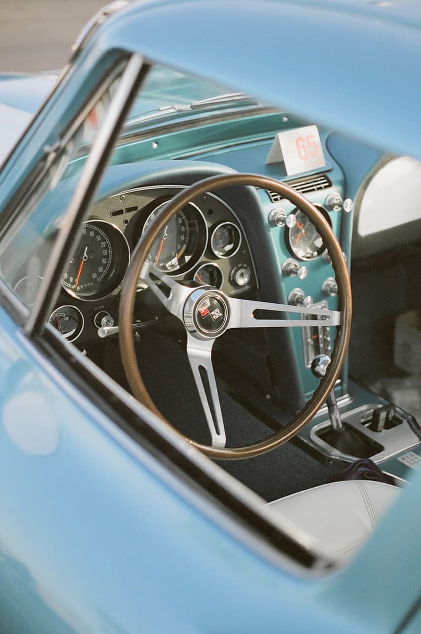 Blue Corvette C2 interior with a wooden steering wheel, chrome gauges, and a vintage dashboard in portrait view.