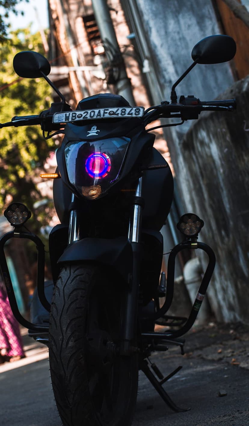 Black custom motorcycle featuring a projector headlight with blue and pink LED accents and thick front tires.