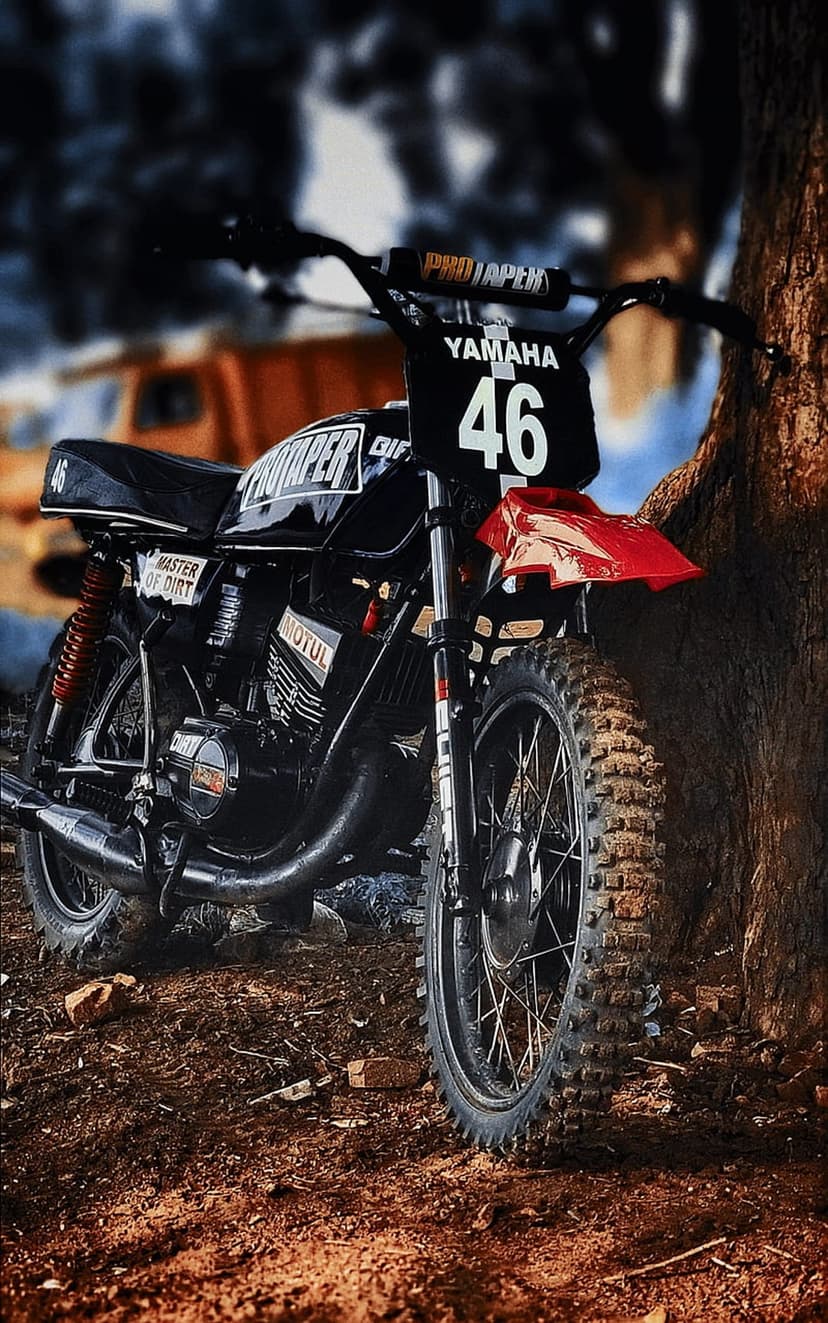 Vintage Yamaha dirt bike with number 46 and red fender leaning against a textured tree in a natural setting.