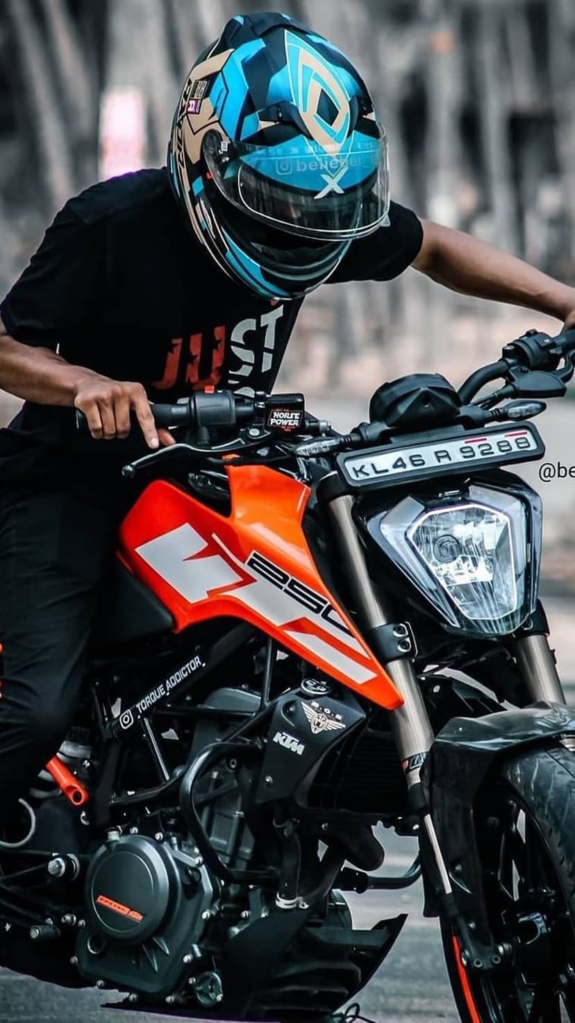 Motorcyclist in a blue patterned helmet sits on an orange KTM 250 bike showing the license plate and 250 decal.