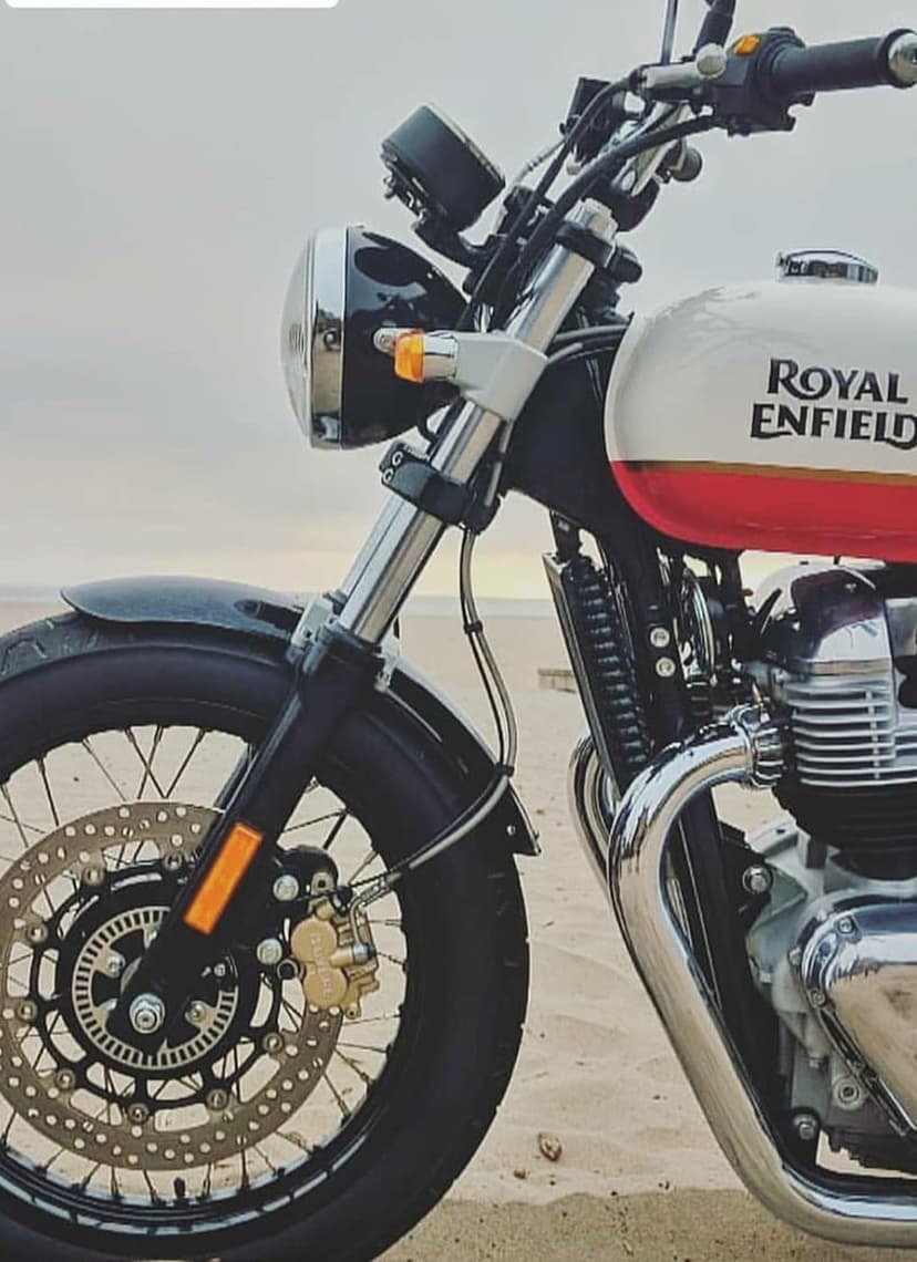 Royal Enfield motorcycle with chrome accents on a sandy beach under a cloudy sky with ocean waves in the distance.