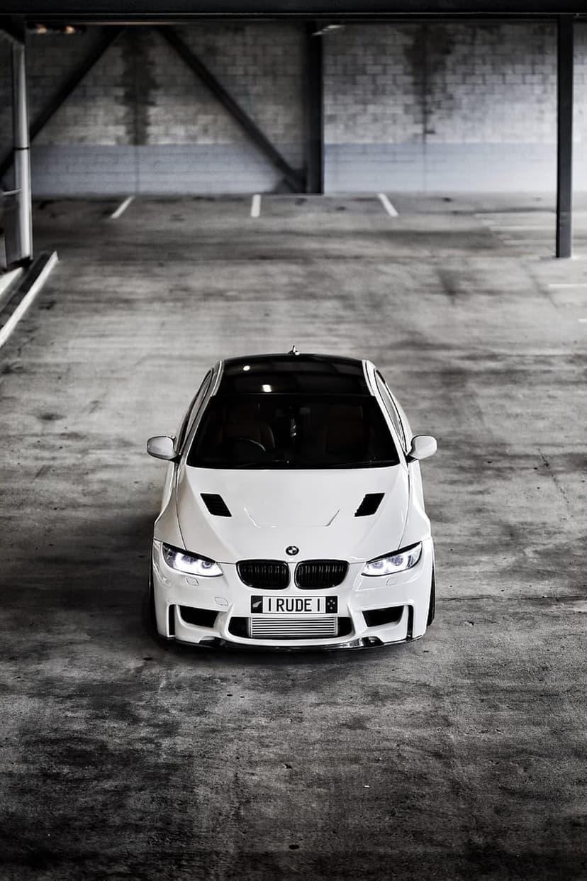 White BMW M3 sports sedan with a black roof parked in a concrete garage, featuring aggressive hood vents and grill.