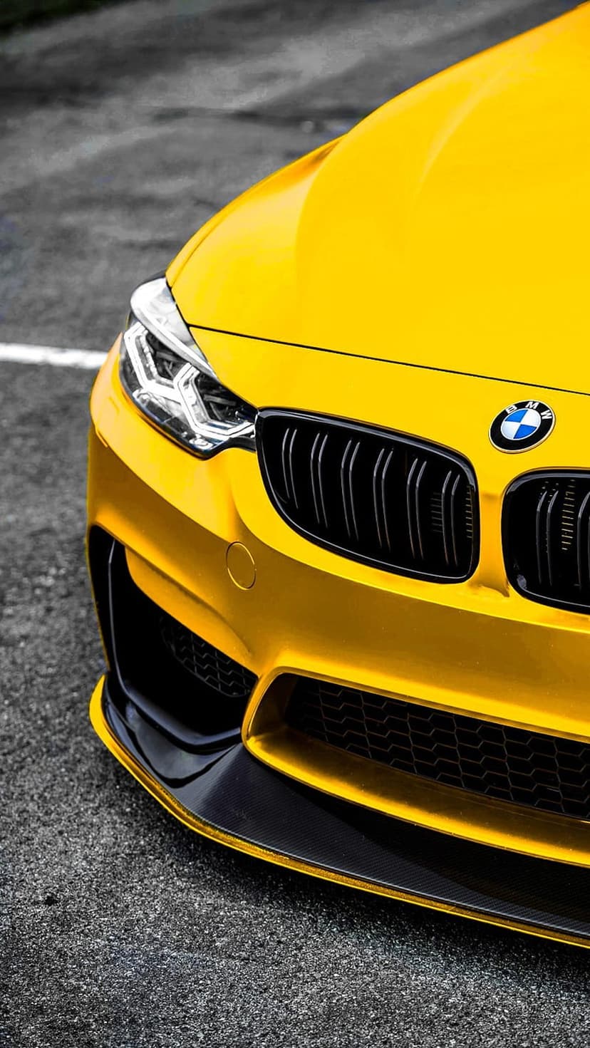 BMW M4 front headlight and kidney grille with yellow paint and carbon fiber details in a close-up automotive shot.