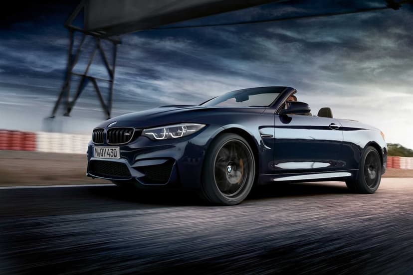 Dark blue BMW M4 Convertible driving fast on a racetrack under a dramatic cloudy sky at dusk.